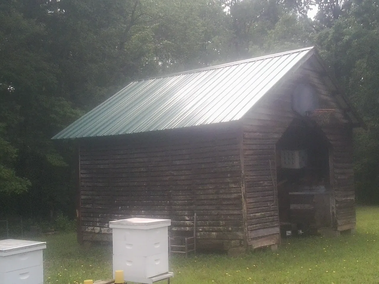 Green metal roof on a weathered barn beside stacked beehives in Reynolds