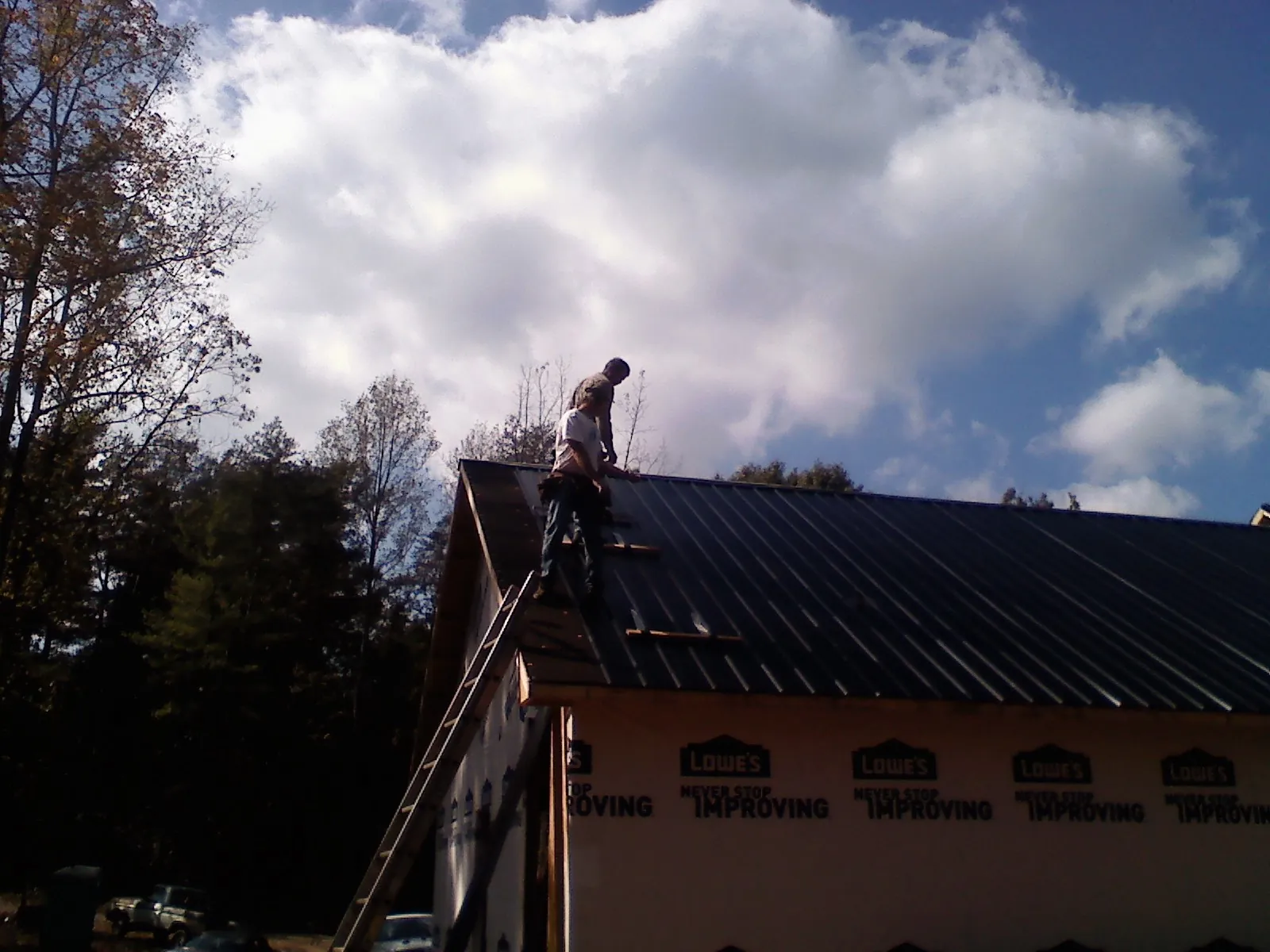 Roofer fastening dark metal panels high against a cloudy sky, from a Roof Inspection job in Reynolds