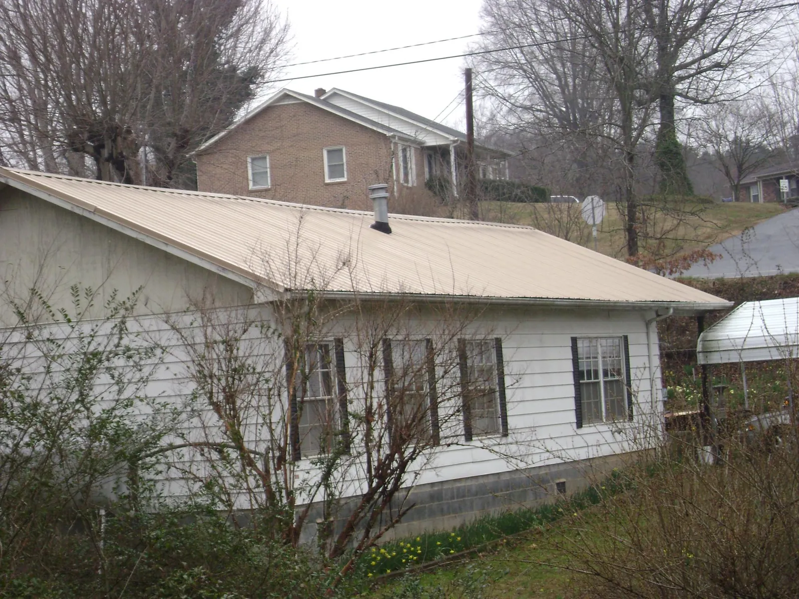 Tan metal roof on a white sided house set into a hillside — Commercial Roofing by Roofing Brothers in Reynolds