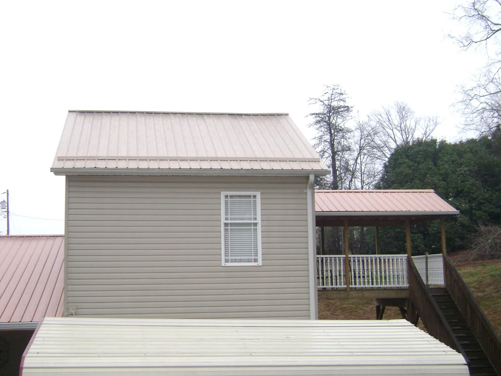 Tan metal roofs on a two story addition and attached porch, from a Roof Replacement job in Reynolds